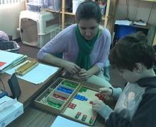 A Montessori teacher guiding a student at a table